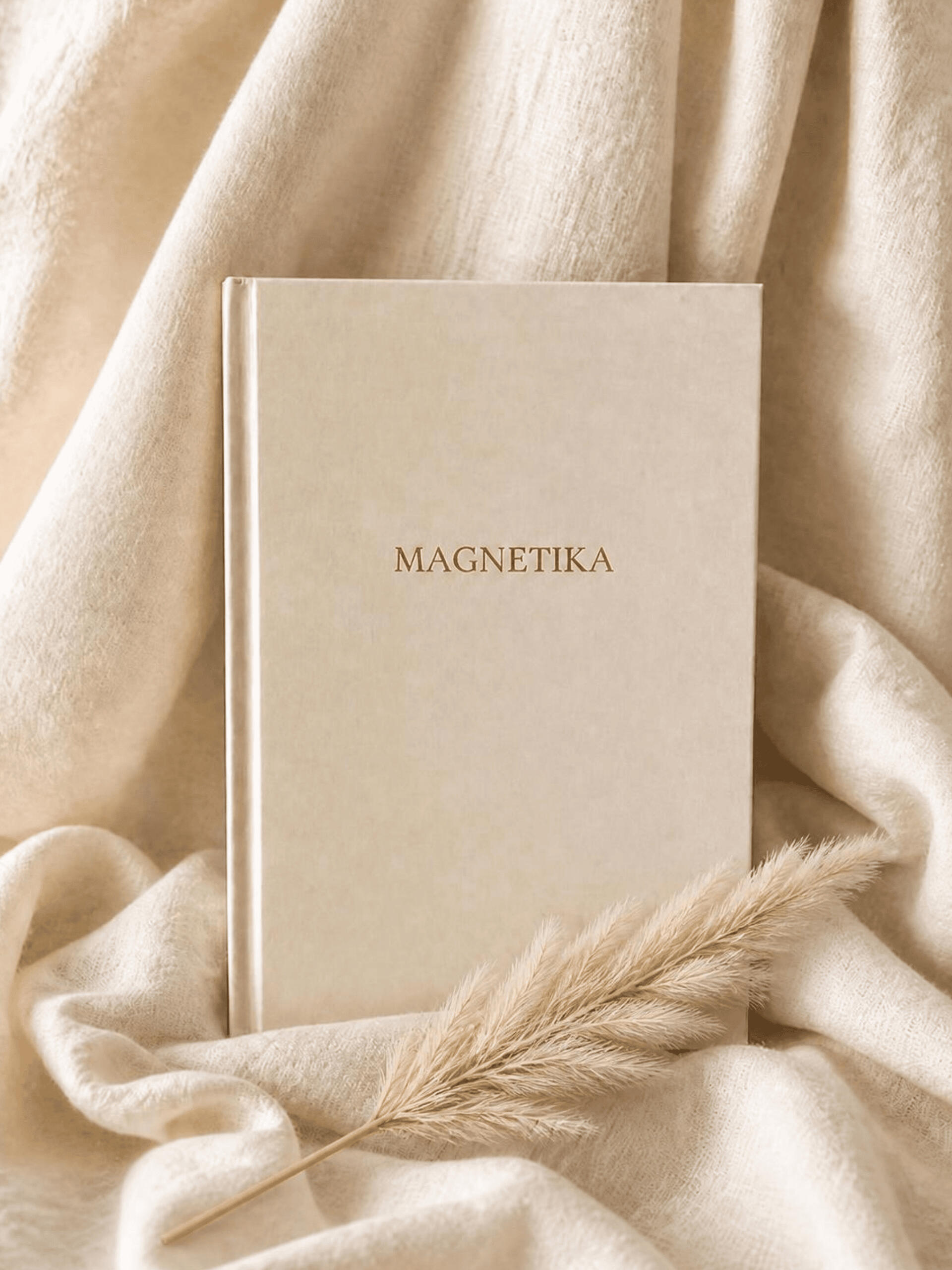 Carnet d'introspection MAGNETIKA à couverture rigide beige, posé sur un tissu clair avec des herbes de pampa